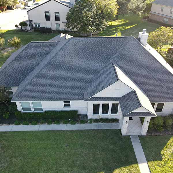 White, mid-class home with new dark gray shingles on its roof installed by Broadway Roofing
